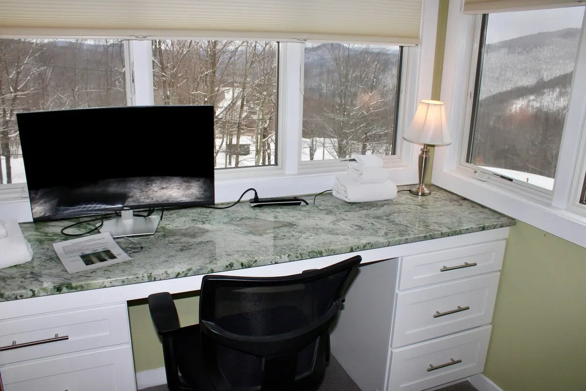 A productive interior space with a marble countertop, computer monitor, lamp, and towels—suggesting both work and relaxation. Natural light pours in, and the setting is serene, making it suitable for extended stays and remote work.