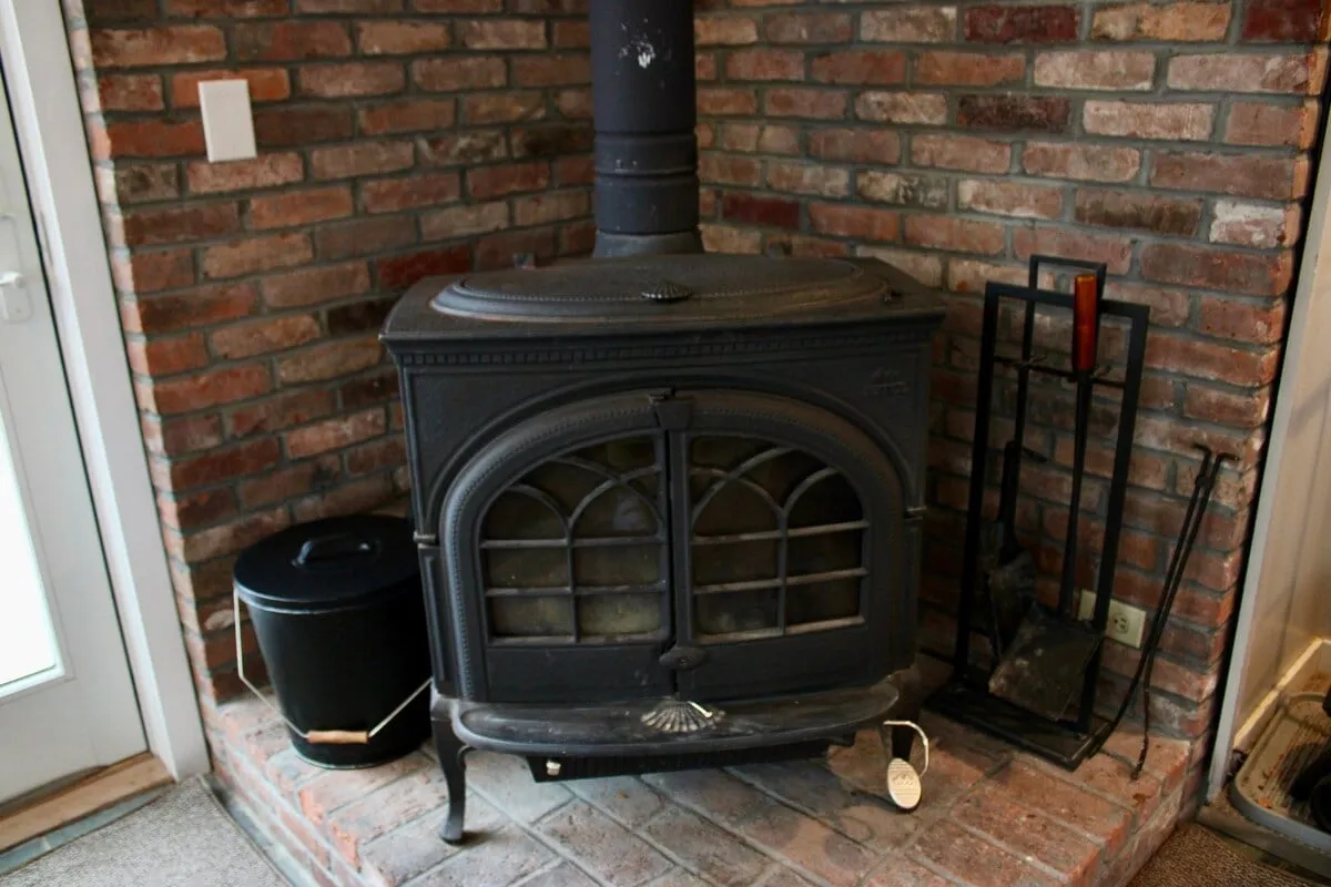 A cozy living area with a wood-burning stove set against a brick wall, surrounded by fireplace tools. The space invites guests to warm up and relax, suggesting a retreat after outdoor activities.