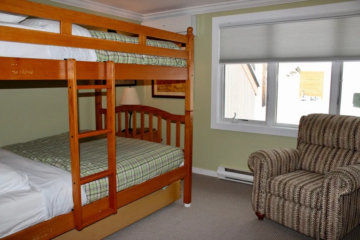 A family-friendly room featuring a bunk bed, a comfortable armchair for reading, and a window allowing in plenty of natural light. The design invites children and adults alike to relax and unwind together after a day of activities.